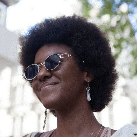 a darksinned woman with afro hair wearing glasses